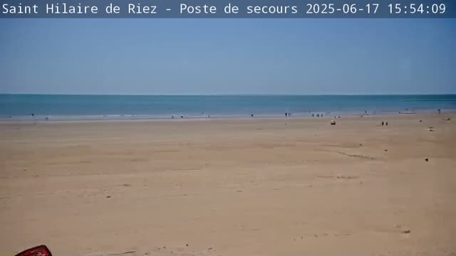 A wide sandy beach stretches to a calm, light-blue ocean under a clear, sunny sky.