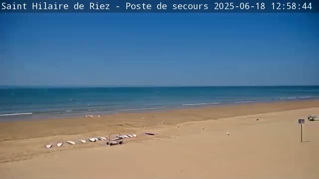 A sandy beach with several sailboards and a calm, blue ocean under a clear sky.