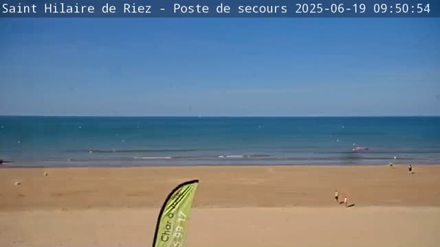 A sandy beach stretches to a calm, blue ocean under a clear sky.