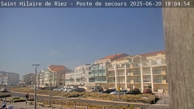 A row of light-colored apartment buildings sits along a road next to a beach on a clear, sunny day.