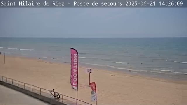 A mostly sunny day at a beach with calm waves, a sandy shore, and a bicycle parked near a boardwalk.