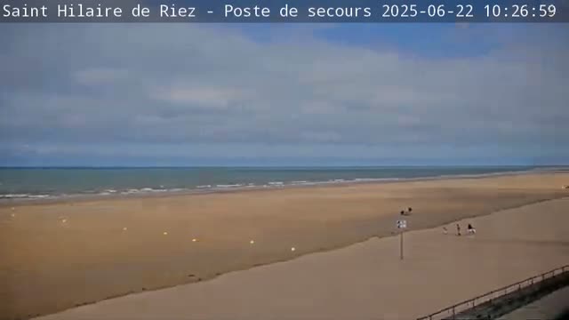 A wide sandy beach stretches to a calm ocean under a mostly cloudy sky.
