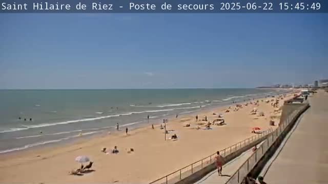 A sandy beach with many people sunbathing and swimming, under a clear blue sky.