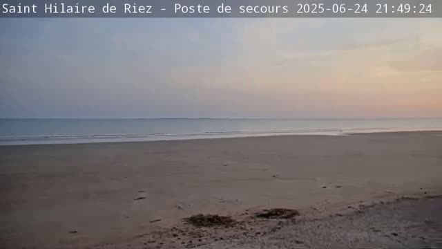 A wide sandy beach stretches to a calm ocean under a pale sunset sky.