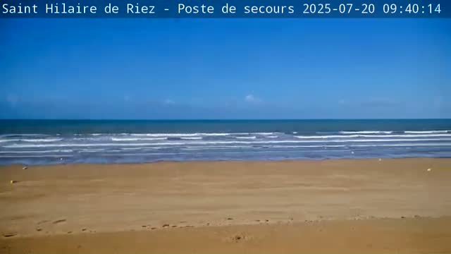 A sandy beach stretches to a calm ocean under a clear blue sky.