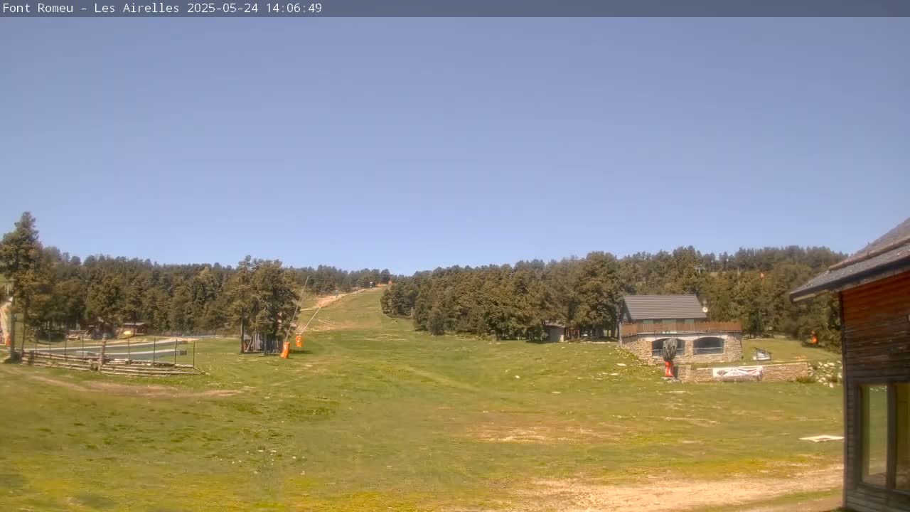 A grassy hillside with a ski lift and several buildings is visible under a clear blue sky.