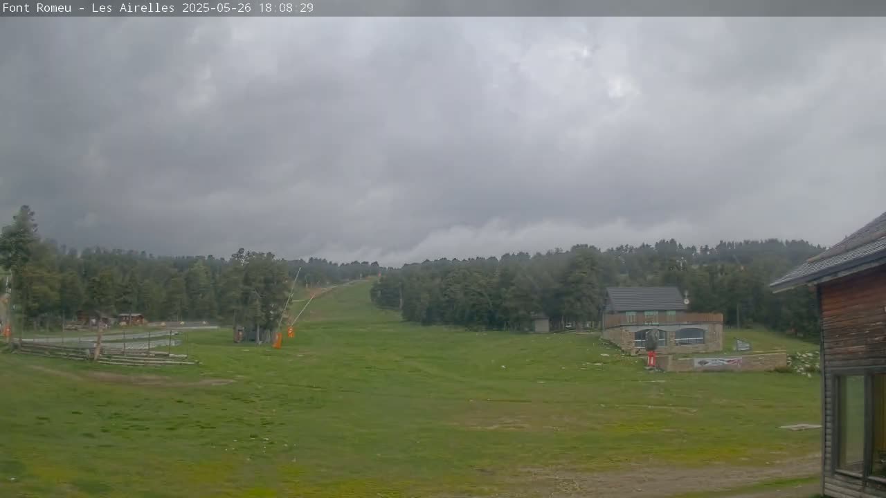 A grassy field with a ski slope and a few buildings is visible under a cloudy sky.