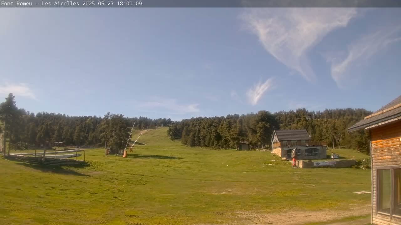 A grassy hillside with a ski lift and several buildings is visible under a mostly clear sky with wispy clouds.
