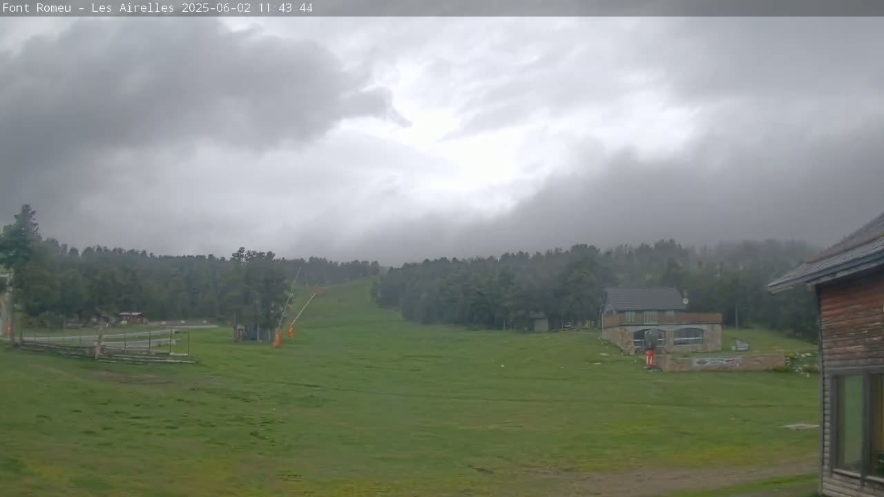A grassy hillside with a ski lift and small buildings is visible under an overcast sky.