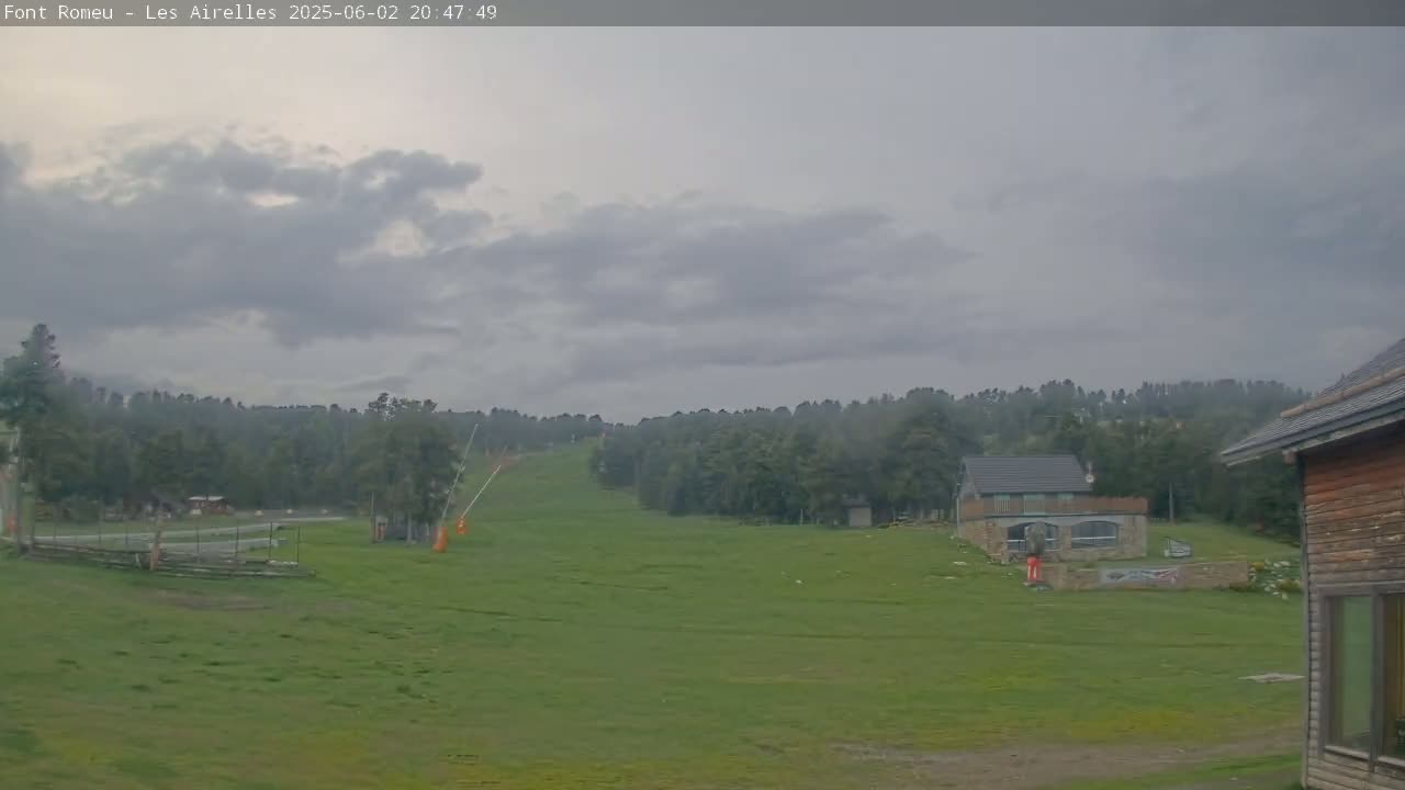 A grassy hillside with a ski lift and small buildings is visible under an overcast sky.
