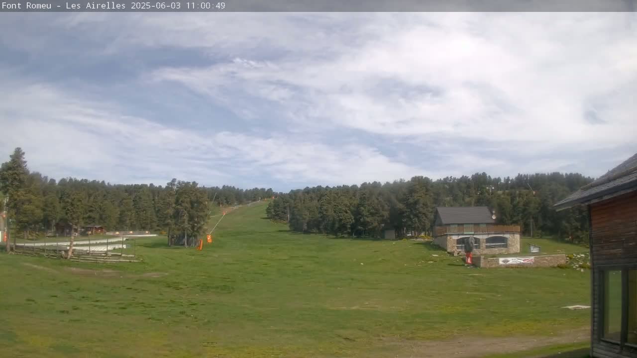 A grassy hillside with a small building and a ski lift in the background under a partly cloudy sky.