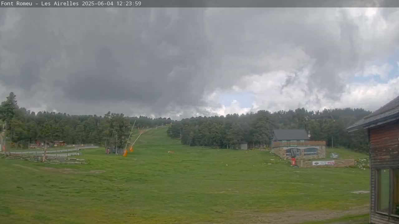 A grassy hillside with a ski lift and buildings is visible under a cloudy sky.