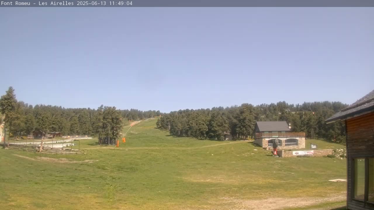 A grassy area with a small building and a ski lift visible in the background under a clear blue sky.