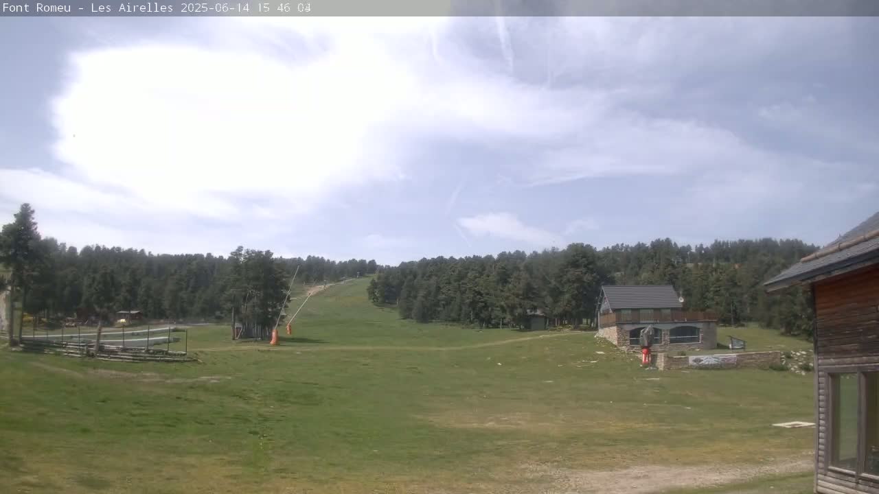 A grassy hillside with a ski lift and a few buildings is visible under a partly cloudy sky.