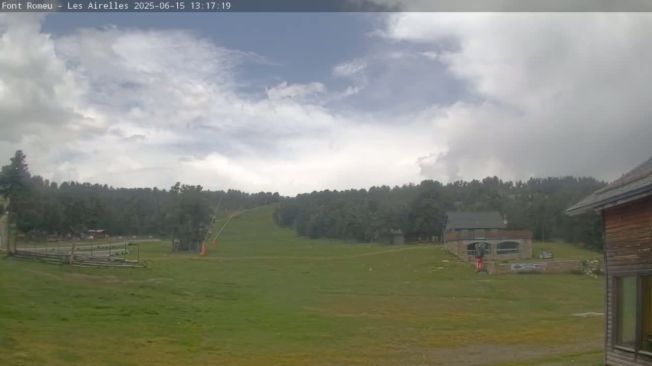 A grassy field with a ski lift in the background, under a partly cloudy sky.