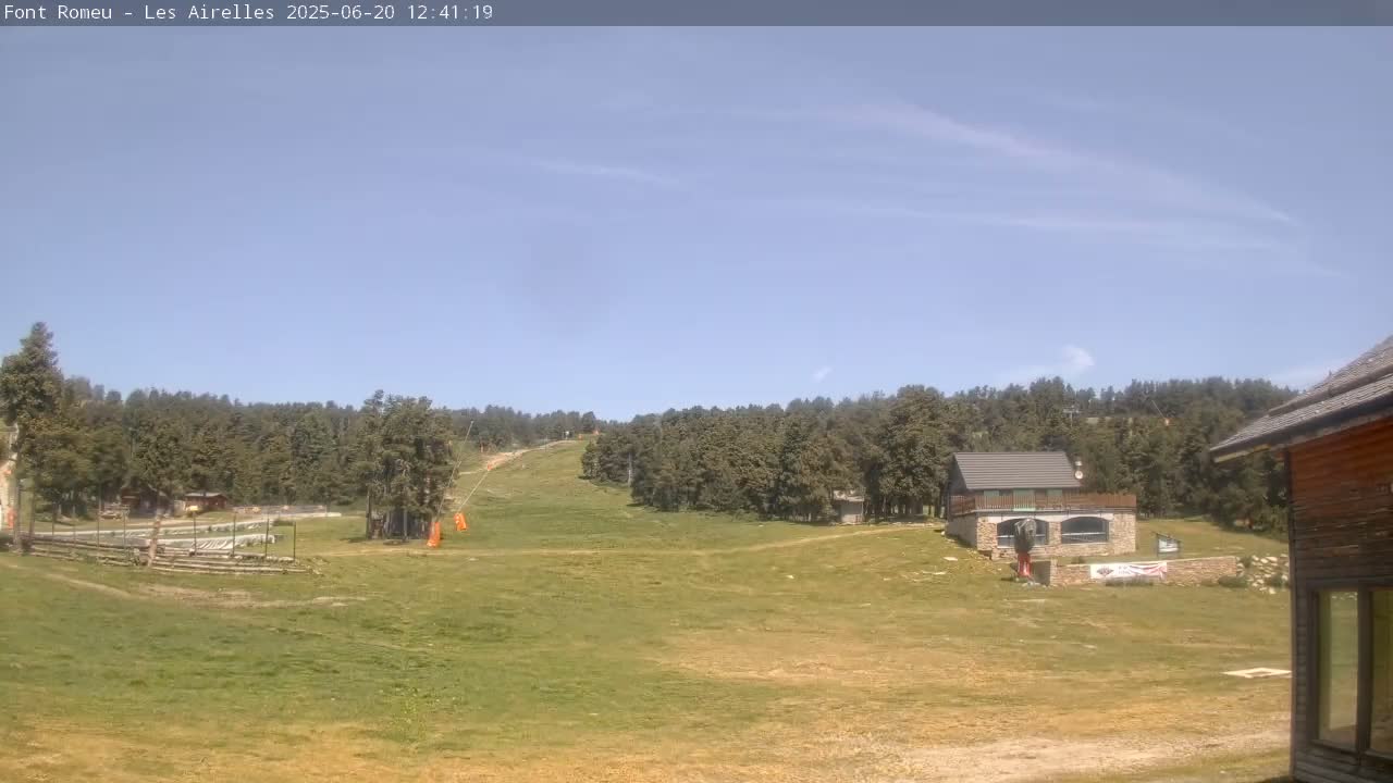 A grassy field with a ski lift and several buildings is visible under a clear blue sky.