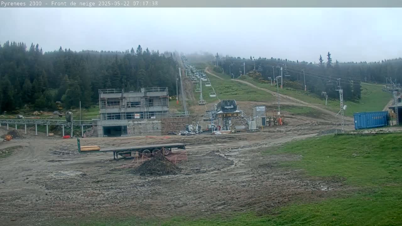 A muddy construction site at a ski resort in a foggy, overcast environment, featuring a chairlift ascending a forested hillside.