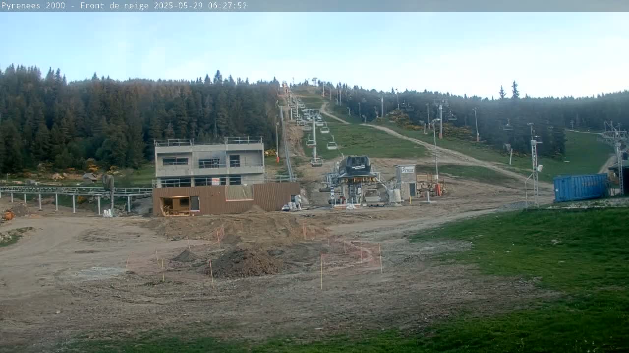 A ski lift and unfinished buildings are situated on a mostly barren hillside, under a clear sky.