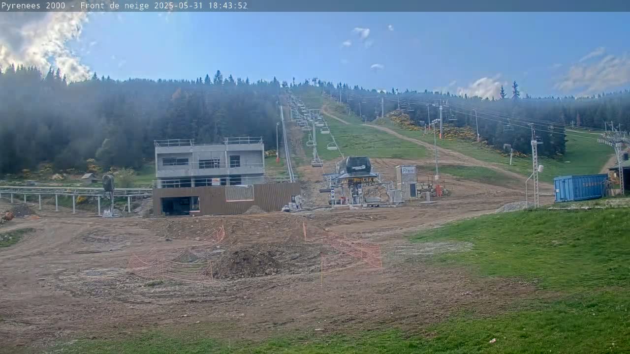 A mostly clear sky looks over a ski lift and partially-constructed buildings on a grassy hillside, with significant earthworks underway.
