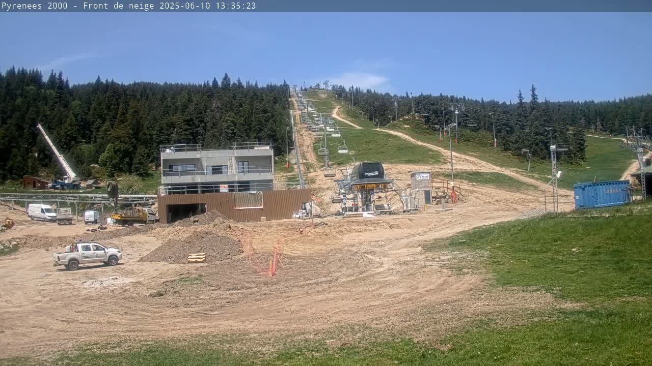 A ski lift and construction site are visible on a sunny day, surrounded by a forested mountainside.