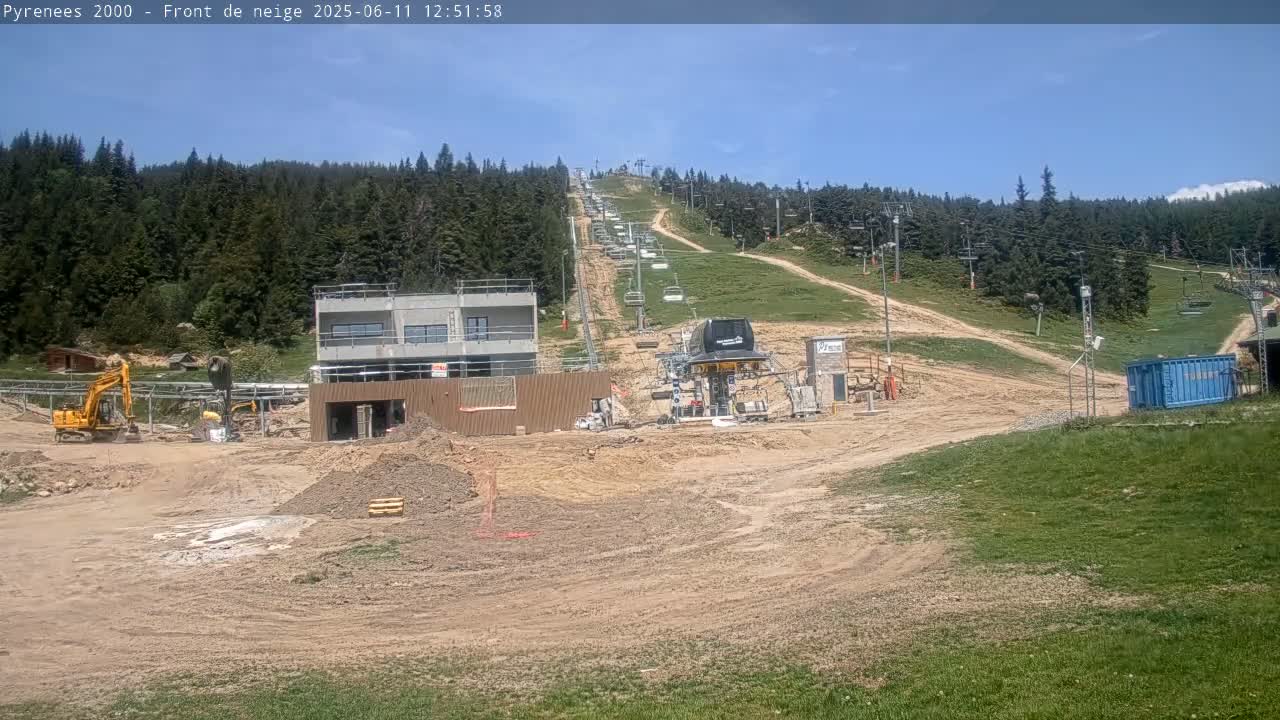 A construction site with heavy machinery near a ski lift ascending a mountain under a mostly sunny sky.