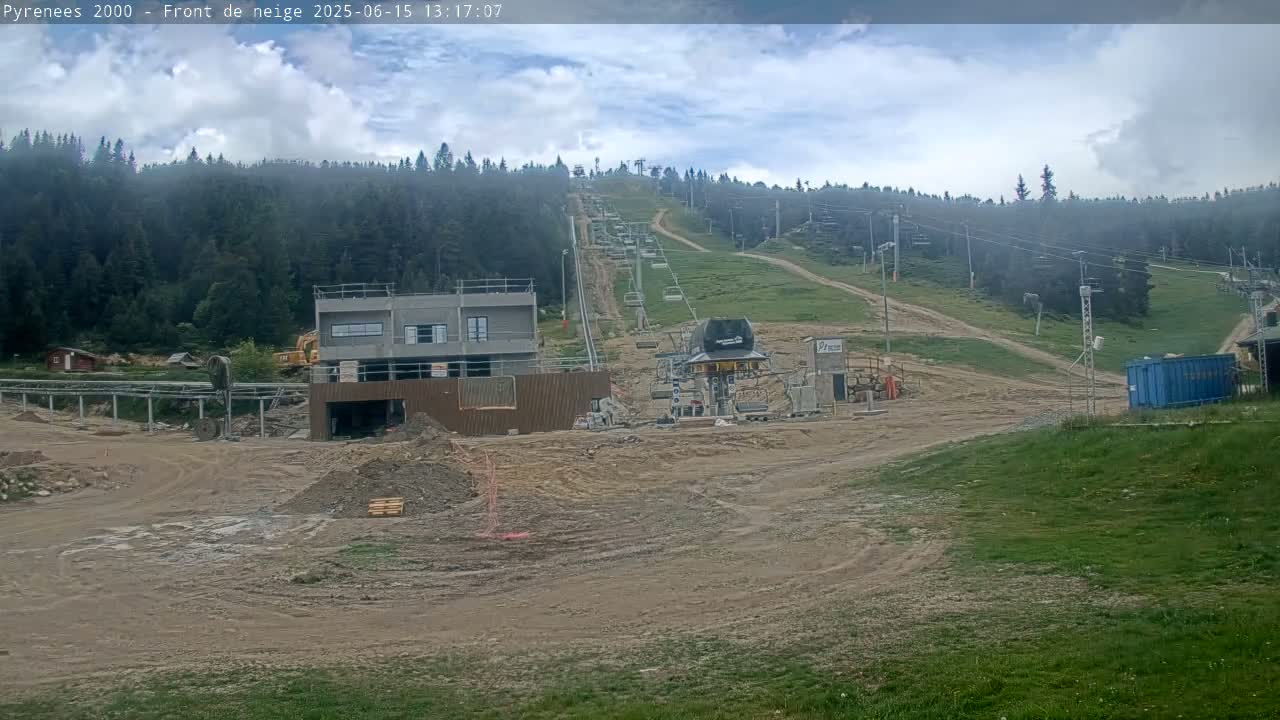 A mostly cloudy day reveals a ski lift under construction in a mountainous area, with a partially built structure and piles of dirt surrounding it.