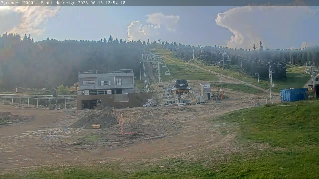 A mostly clear sky with some clouds hangs over a mountain ski lift under construction, with dirt and construction materials visible in the foreground.