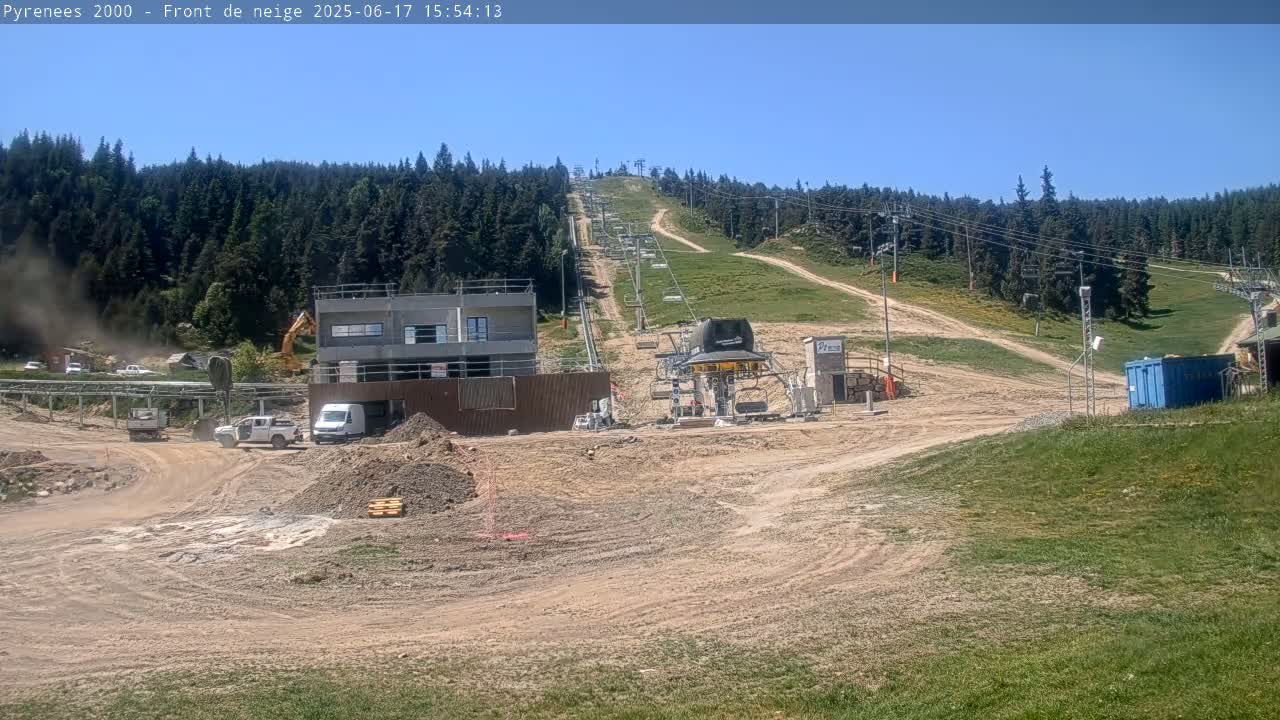 A ski lift under construction is situated on a hill surrounded by a forest, on a sunny day.