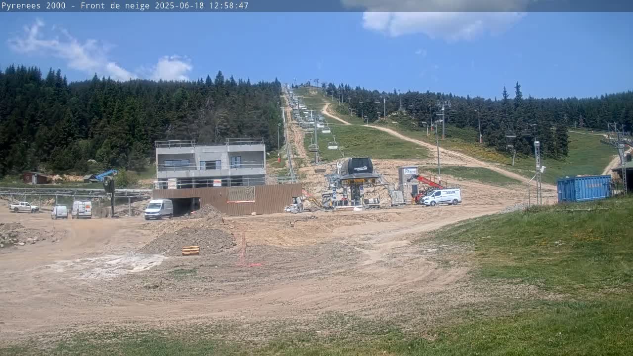 A ski lift under construction is situated on a hillside surrounded by a forest, under sunny skies.