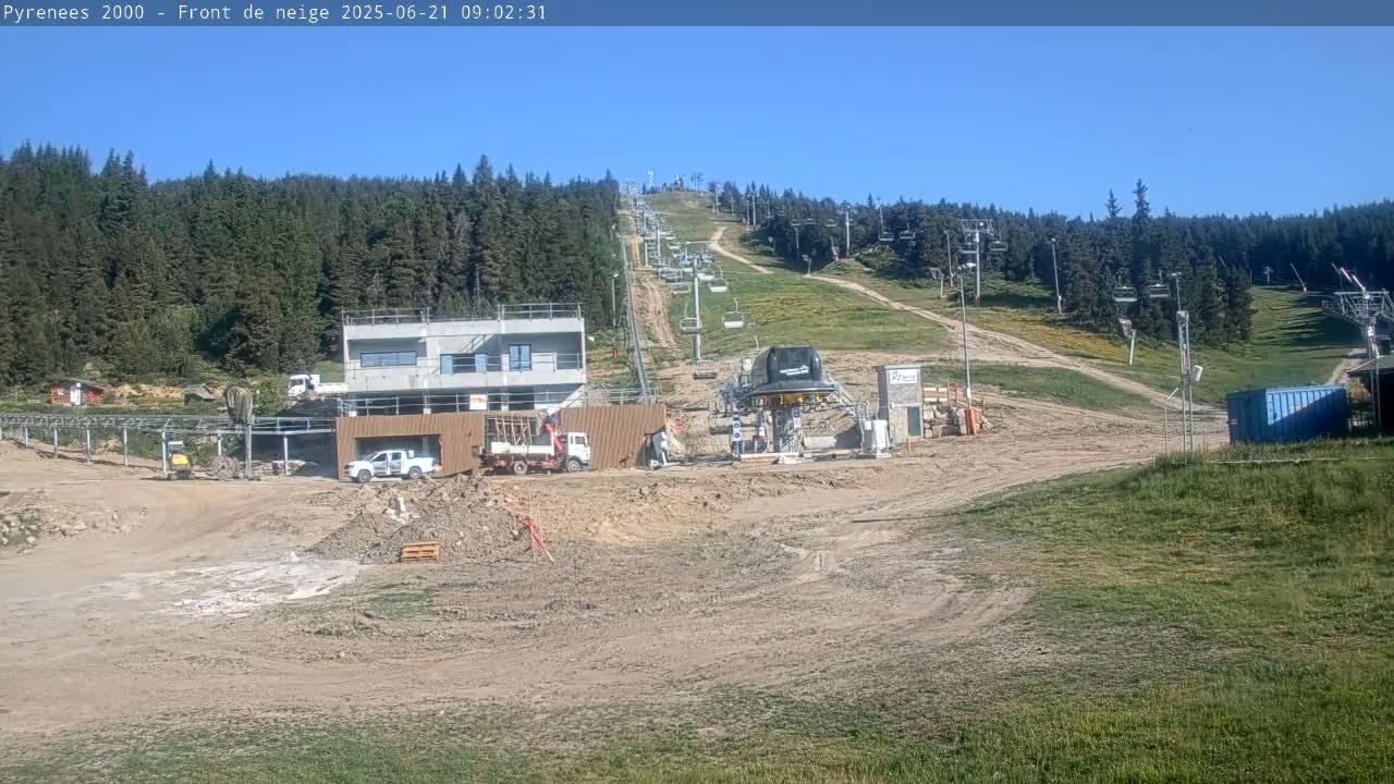 A ski lift and surrounding area are under construction, with several vehicles and building materials present on a mostly clear, sunny day.