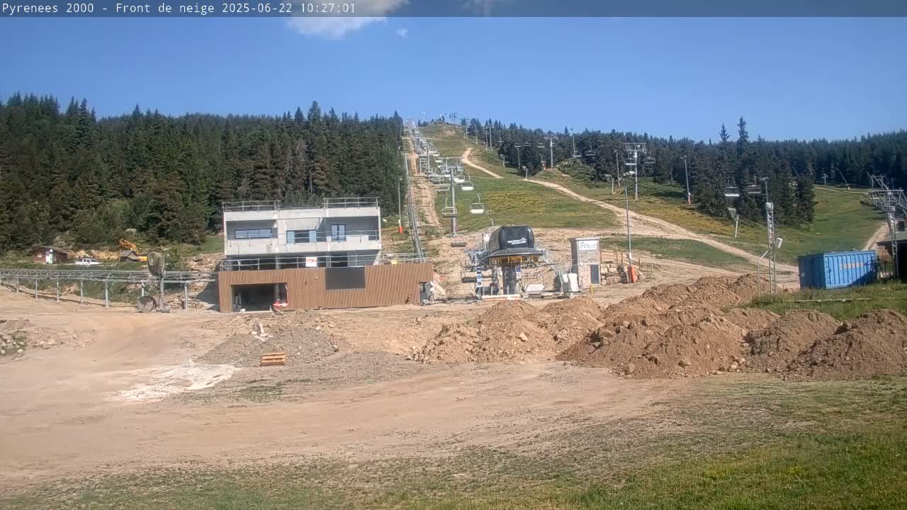 A ski lift and resort under construction are situated on a mountainside on a sunny day, with piles of dirt and construction equipment visible in the foreground.