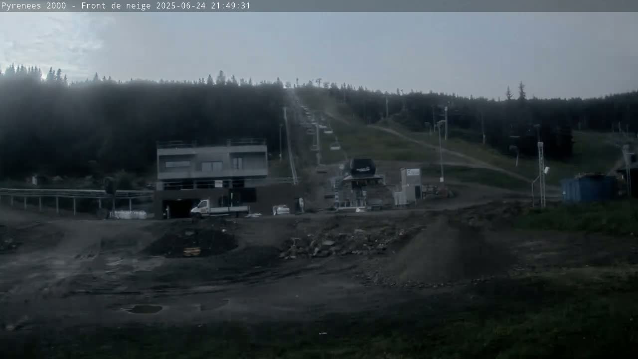 A ski lift ascends a hill covered in dark green vegetation under an overcast sky, with construction equipment and piles of dirt visible in the foreground.