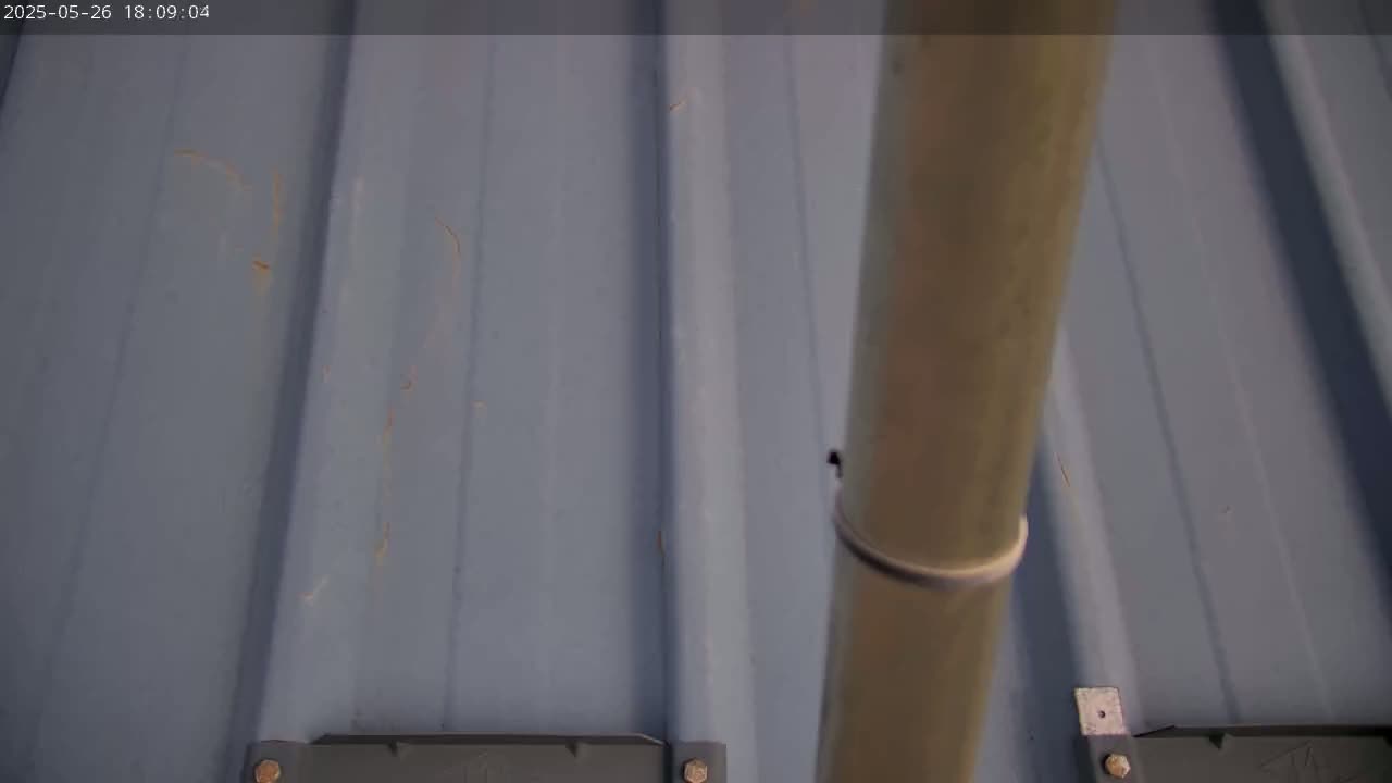 A close-up view shows a light-blue corrugated metal roof with a downspout and some minor rust-colored marks.