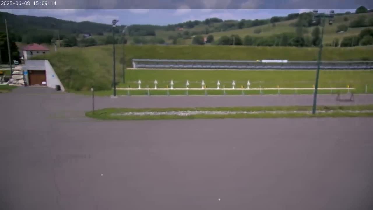 A mostly cloudy day reveals a shooting range with targets set up in front of a grassy embankment and a building in the background.