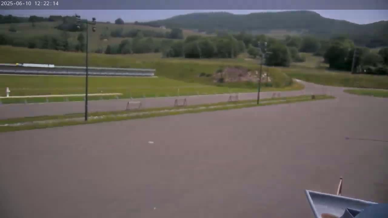 A paved area with a track and grassy fields, under an overcast sky, with distant hills in the background.