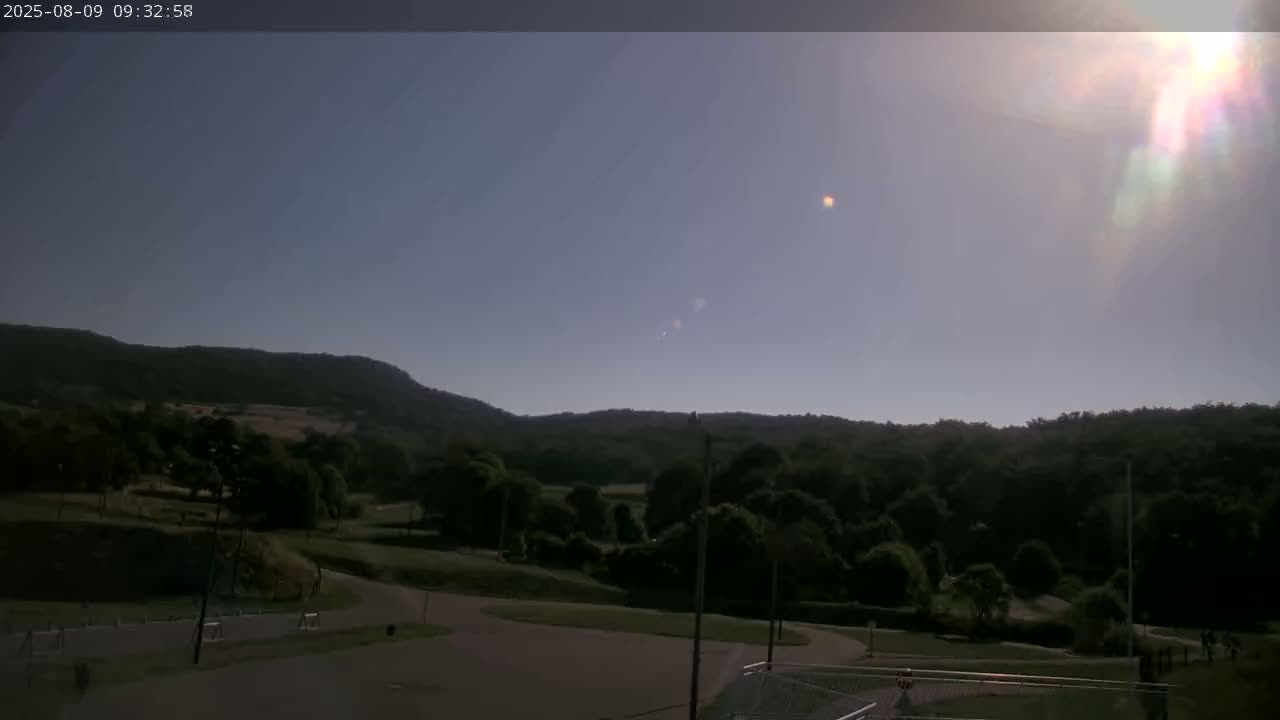 A sunny day reveals a landscape of green hills, trees, and a paved area, possibly a park or parking lot.