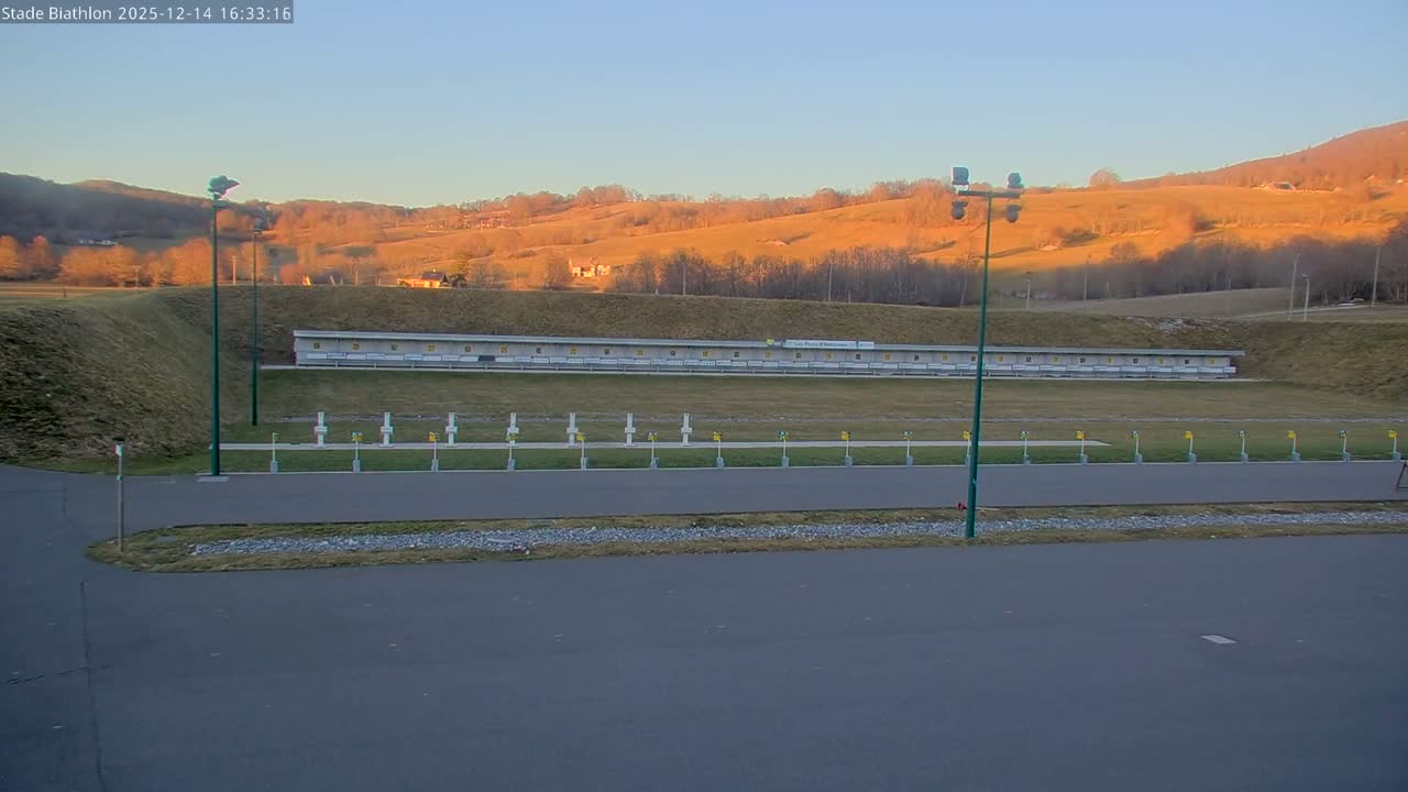 A snow-covered outdoor sports area, featuring rows of white cross-shaped targets and square markers, along with tall floodlight poles, lies under a uniformly gray, overcast sky with light snow actively falling.