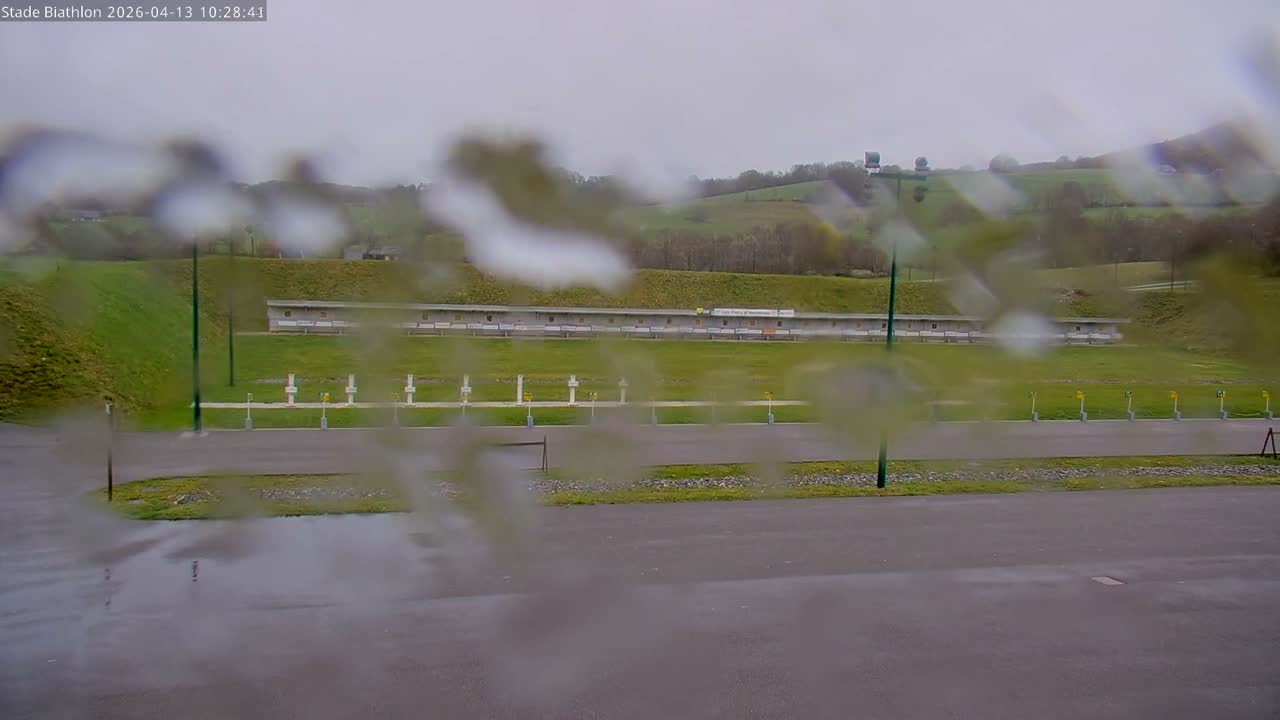 A snow-covered outdoor sports area, featuring rows of white cross-shaped targets and square markers, along with tall floodlight poles, lies under a uniformly gray, overcast sky with light snow actively falling.