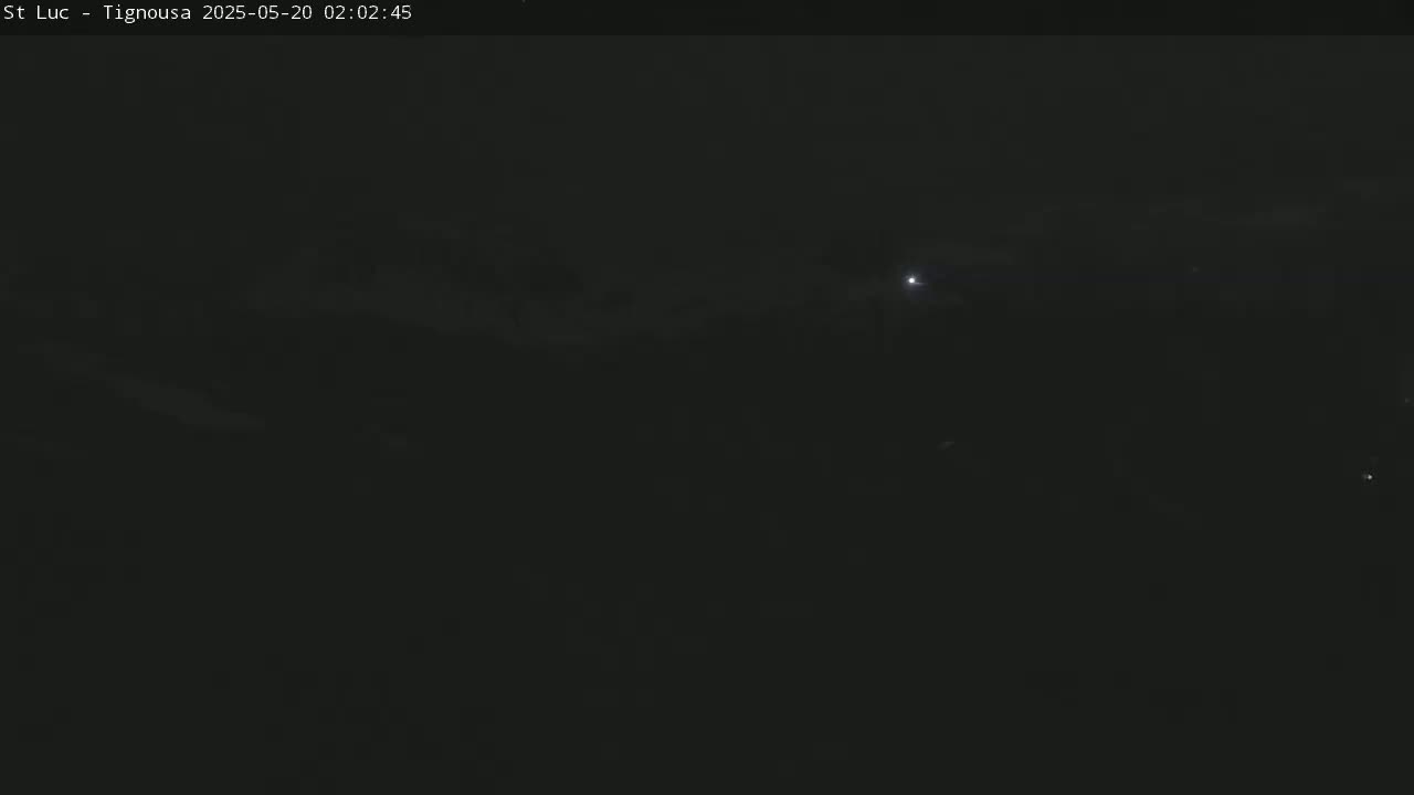 A dark, nighttime scene shows a few faint lights in the distance under a mostly clear sky.