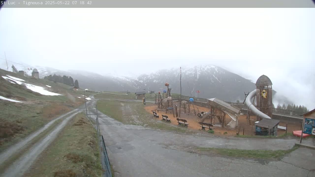A playground sits on a hilltop overlooking snow-capped mountains in foggy weather.