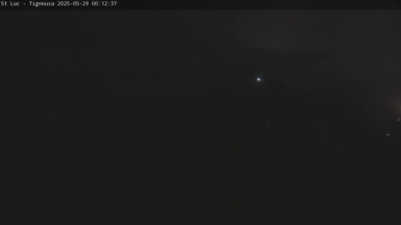 A dark, nighttime scene shows a few faint lights in the distance under a mostly clear sky.