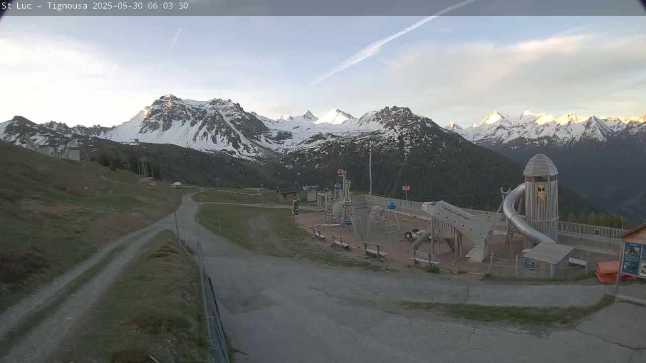 A playground sits below a mountain range capped with snow under a mostly clear sky.