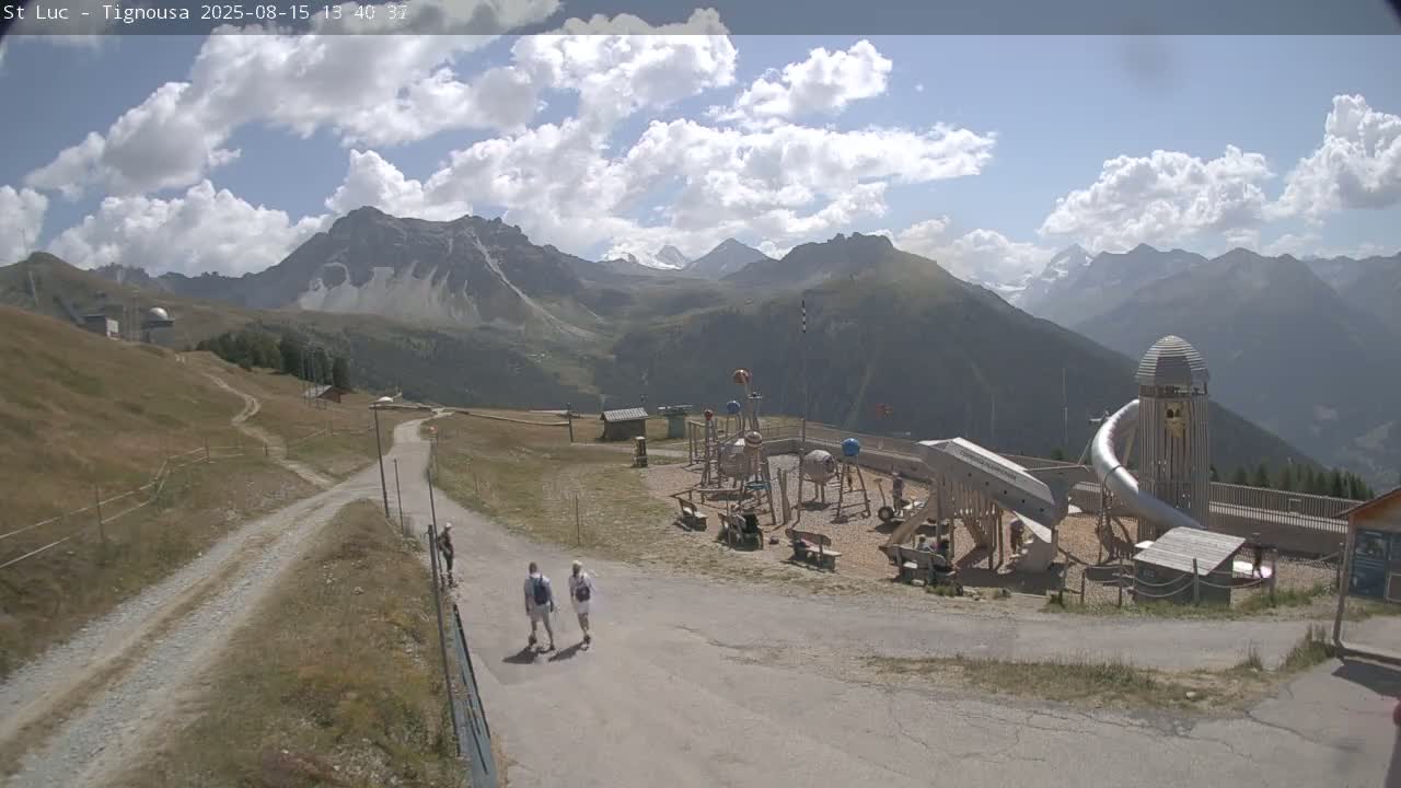 A playground sits on a grassy hill overlooking a mountain range on a clear, sunny day.