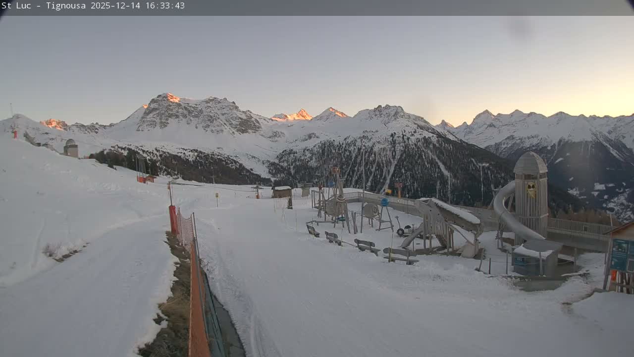 A snow-covered mountain ski area with a children's playground is depicted under a partly cloudy sky with sunlight breaking through.