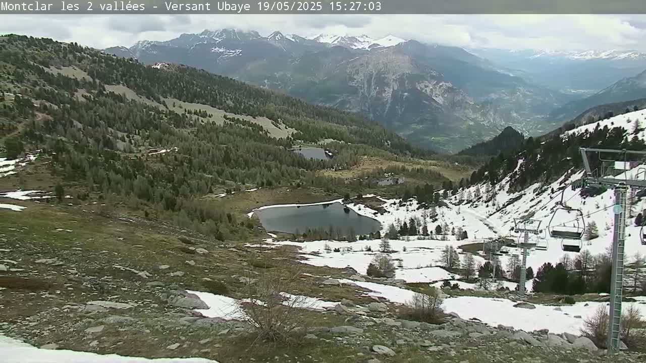 A mountain vista with patches of snow, two small lakes, and a chairlift, under partly cloudy skies.