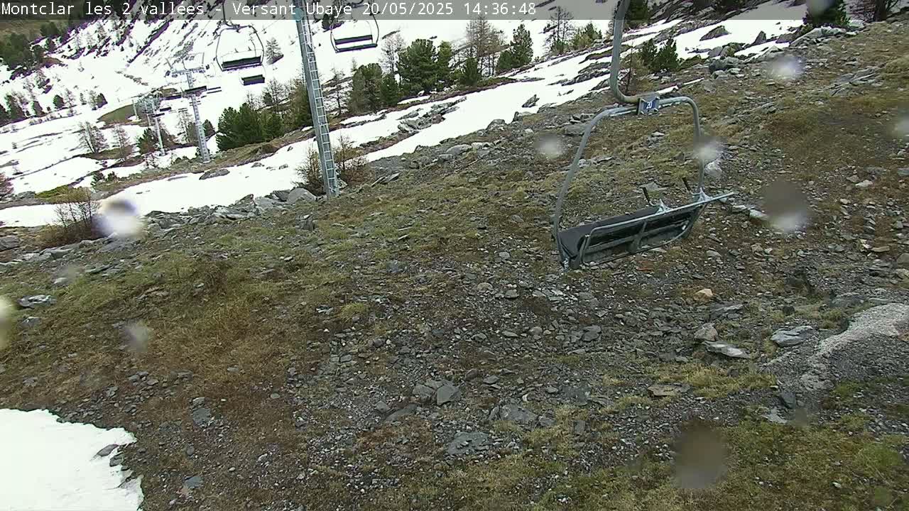 A rocky, grassy hillside with patches of snow, a chairlift in the foreground, and rain falling.