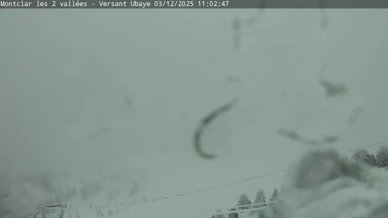 A very blurry, snow-covered outdoor landscape is seen through a precipitation-covered camera lens, indicating heavy snowfall or dense fog with extremely low visibility.