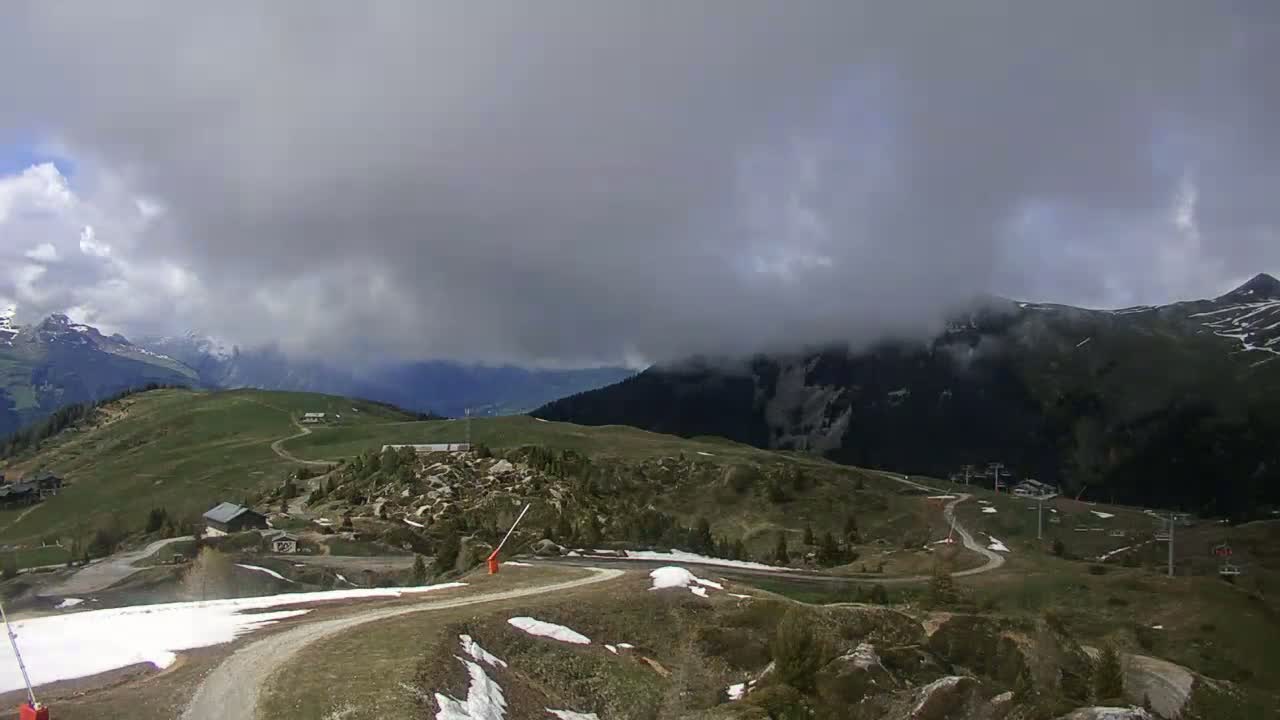 A mountain landscape with patchy snow, under a cloudy sky.