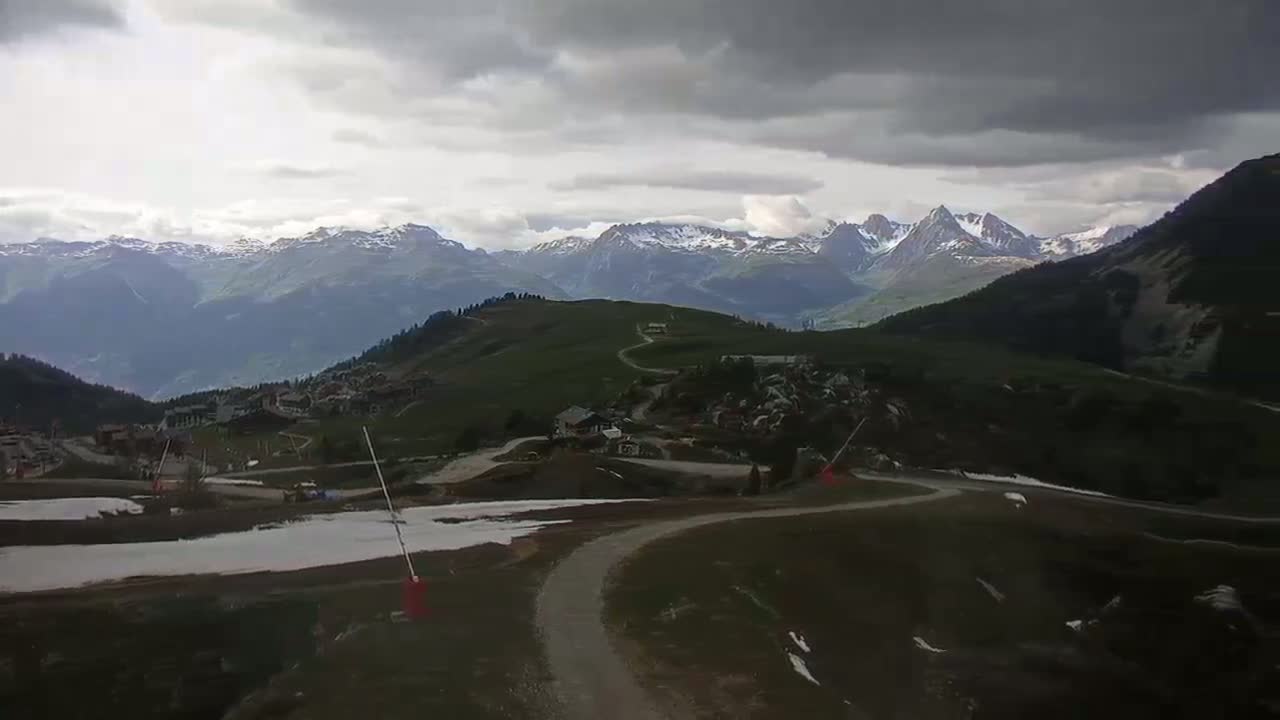 A winding road leads through a mountainous landscape with patches of snow under an overcast sky.