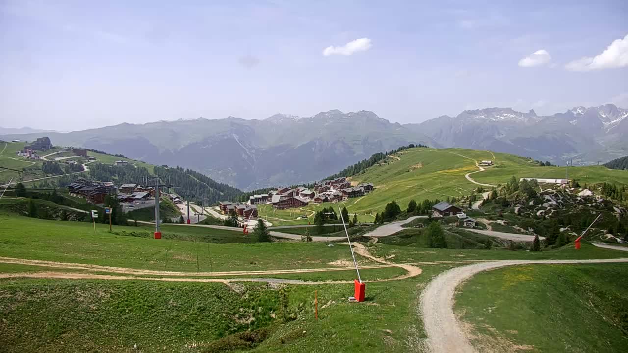 A mountain village nestled in a valley, with green hills and a partly cloudy sky.